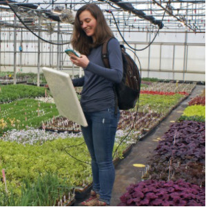 Woman stands in horticulture building using technology to analyze her plants