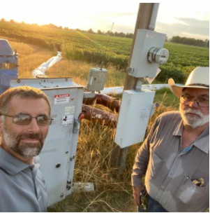 Two men stand in a field looking at irrigation lines