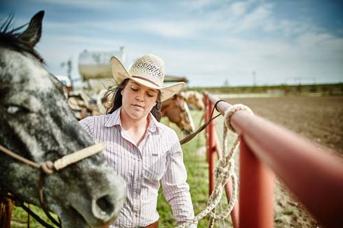 Young woman farmer on cattle ranch land with a horse.