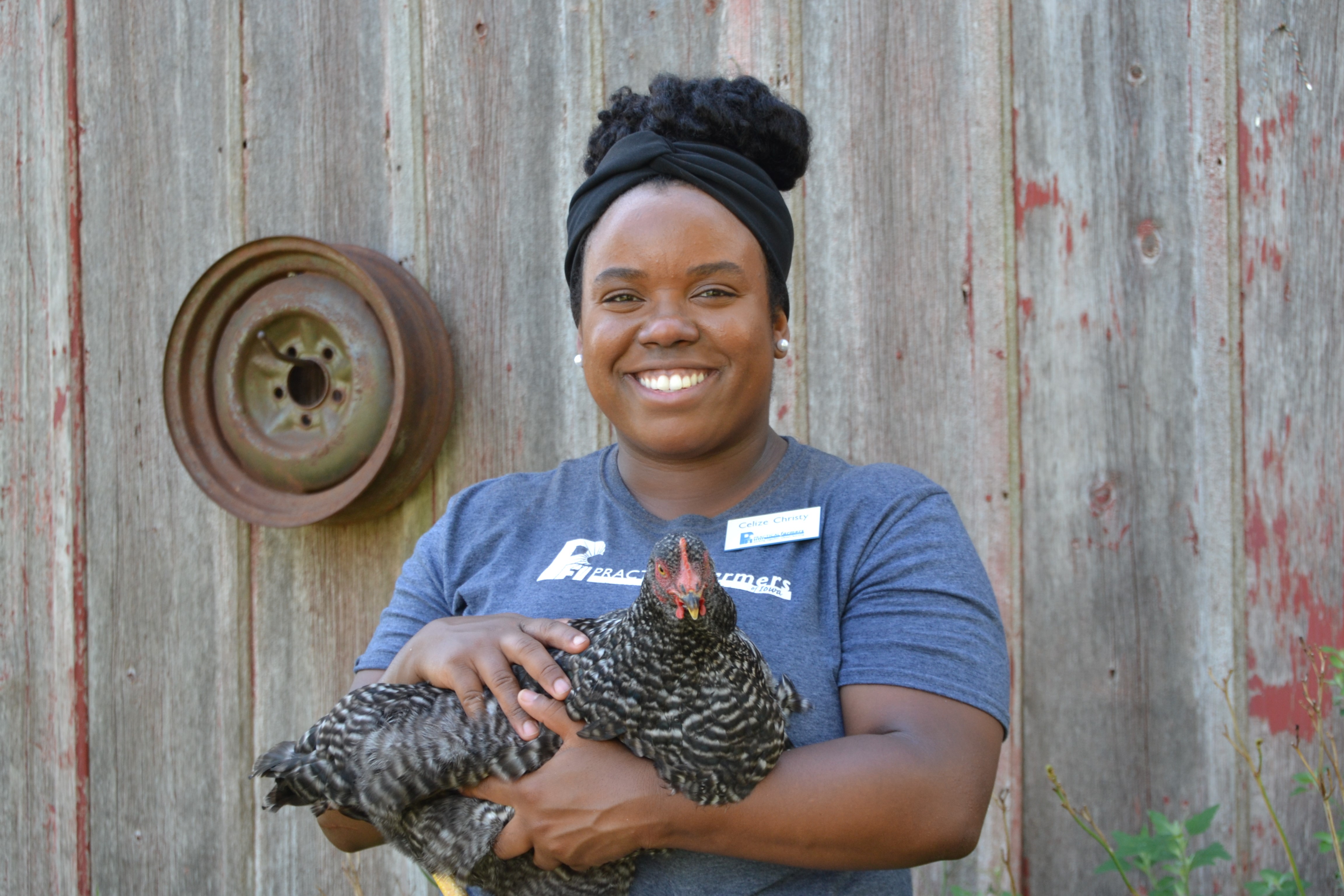 Celize Christy poses with a chicken in her arms in front of the wall of a barn.