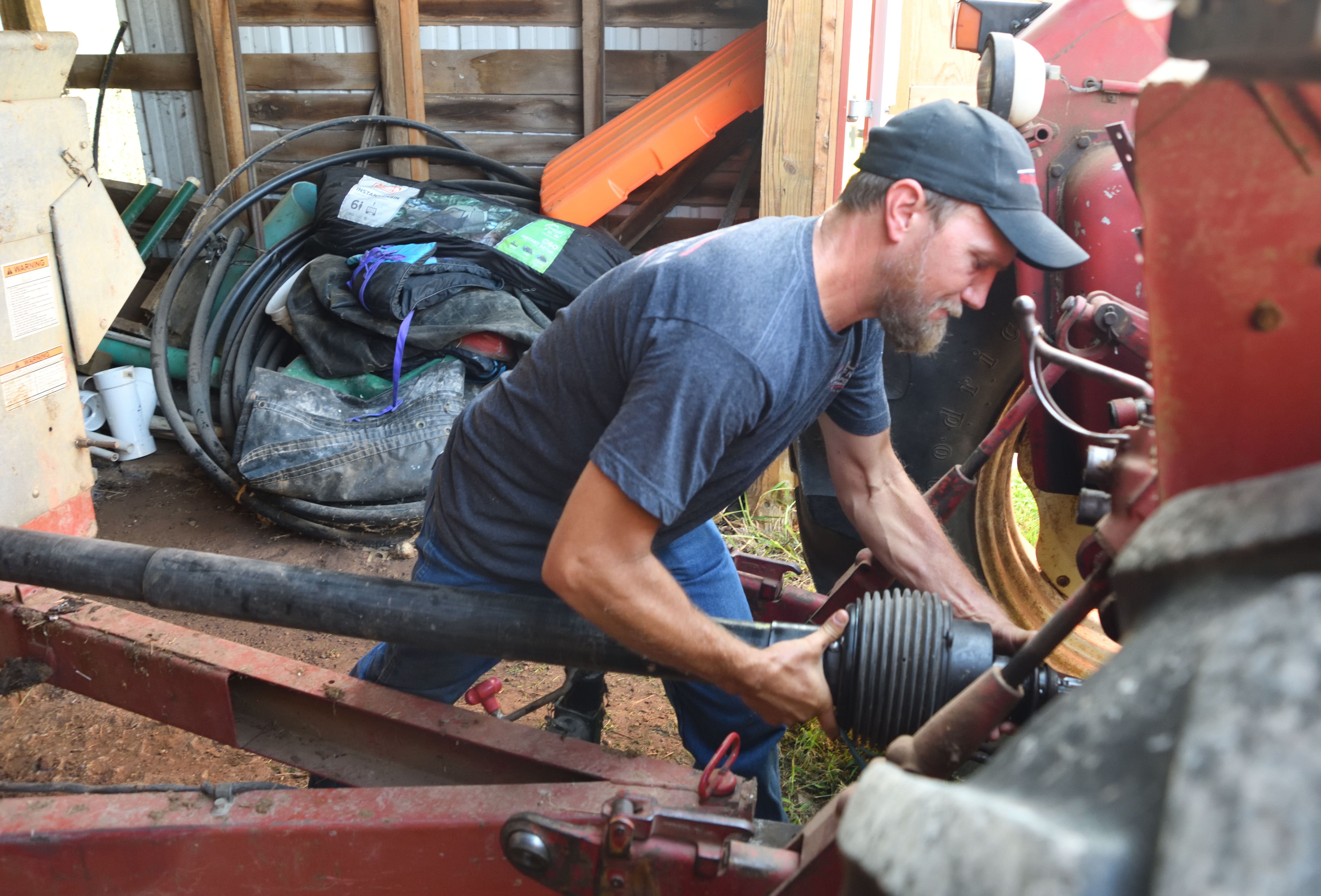 Man in dark clothes attaches mechanical units together, red machinery in foreground