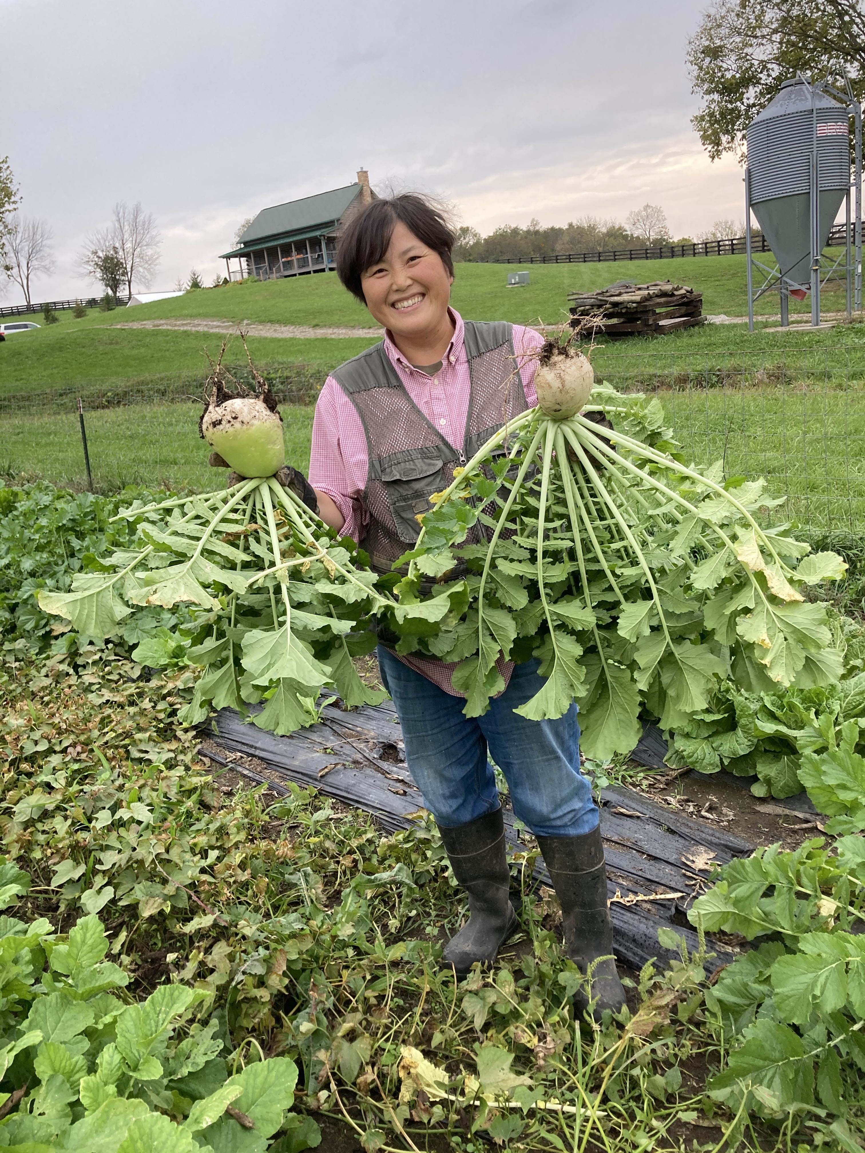 Soonnyoung Min, a beginning farmer in Kentucky, stands in a field holding root vegetable