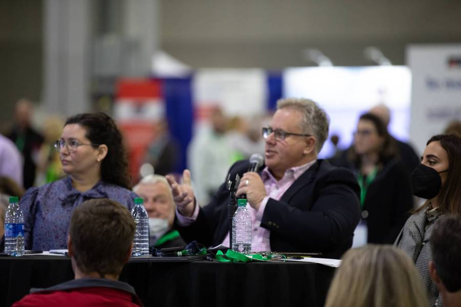 man seated at table speaking in to microphone 