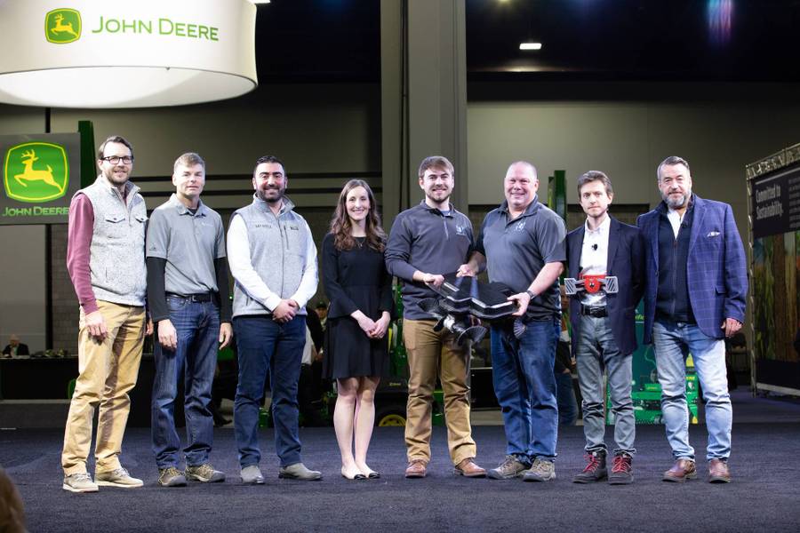 group of 8 people stand on stage, two machines are on display